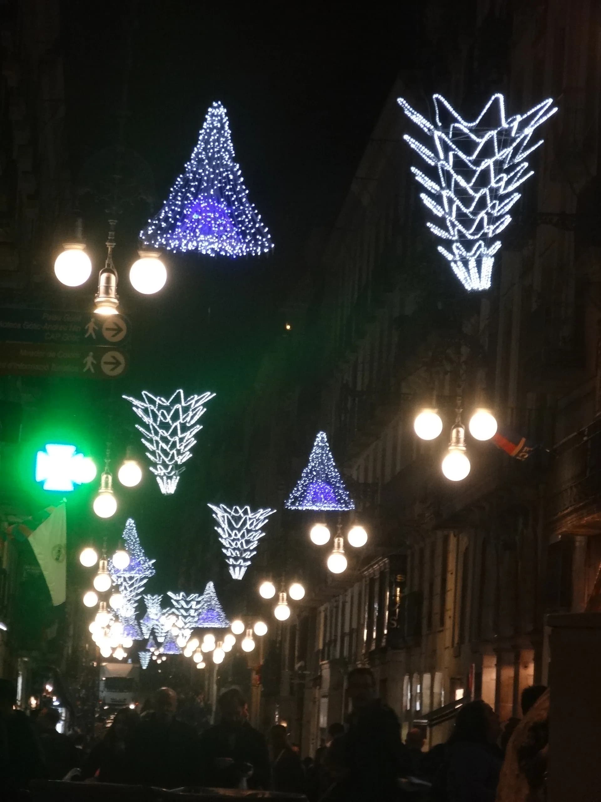 Carrer de Barcelona amb llums de Nadal en forma d'arbre i gent passejant